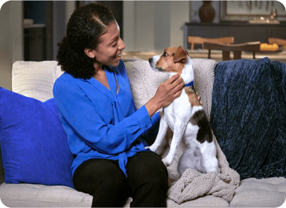 A woman pets her happy dog while sitting on the couch